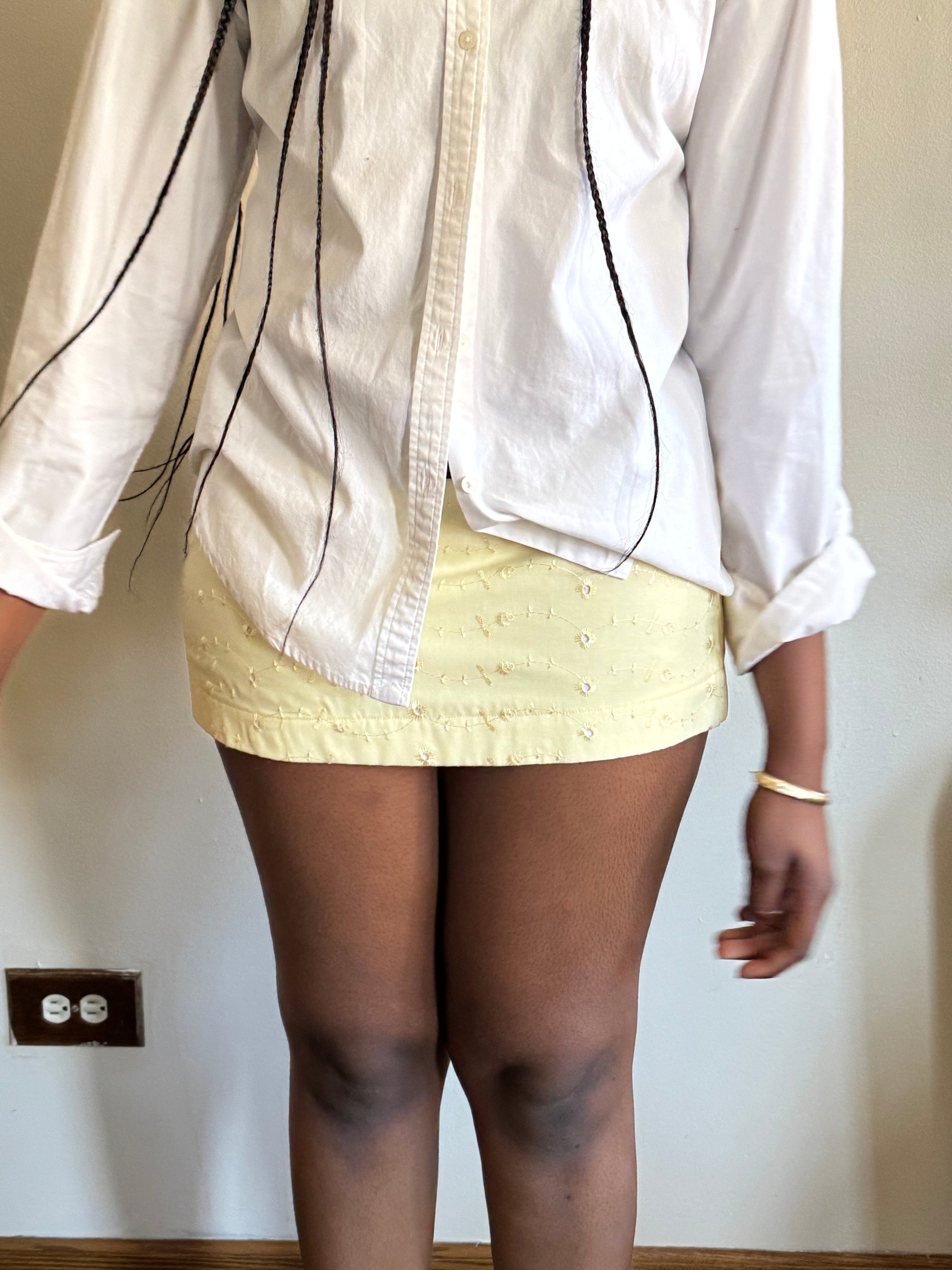 Sculpted yellow eyelet skirt flowing in sunlight, styled for rooftop dinners and gallery visits.

